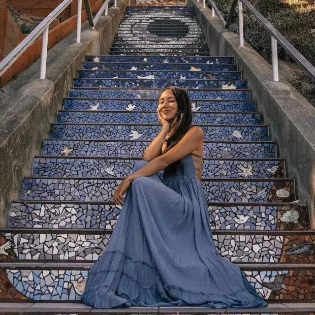 A woman poses sitting on the 16th Avenue tiled stairs in the Sunset neighborhood of San Francisco.